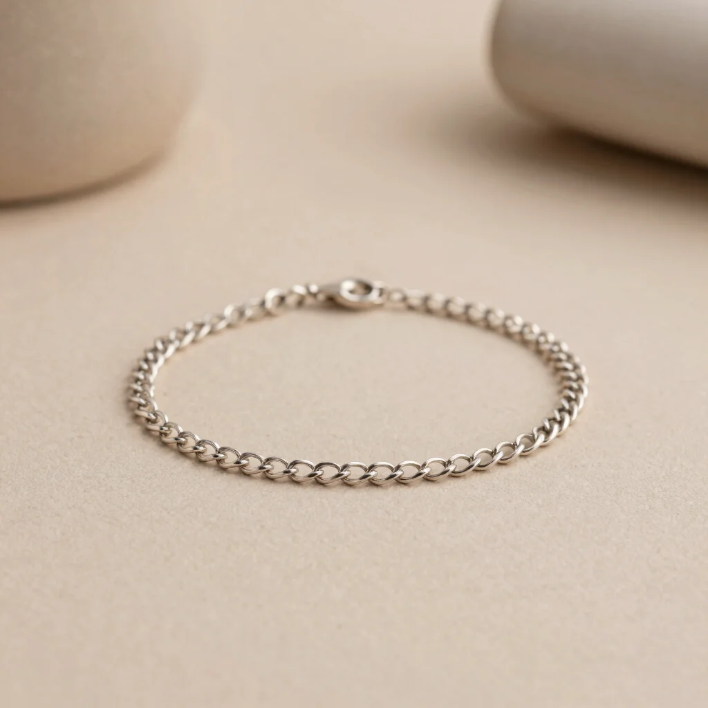 Fine silver-toned chain bracelet on smooth beige stoneware, soft neutral tones, shallow depth of field