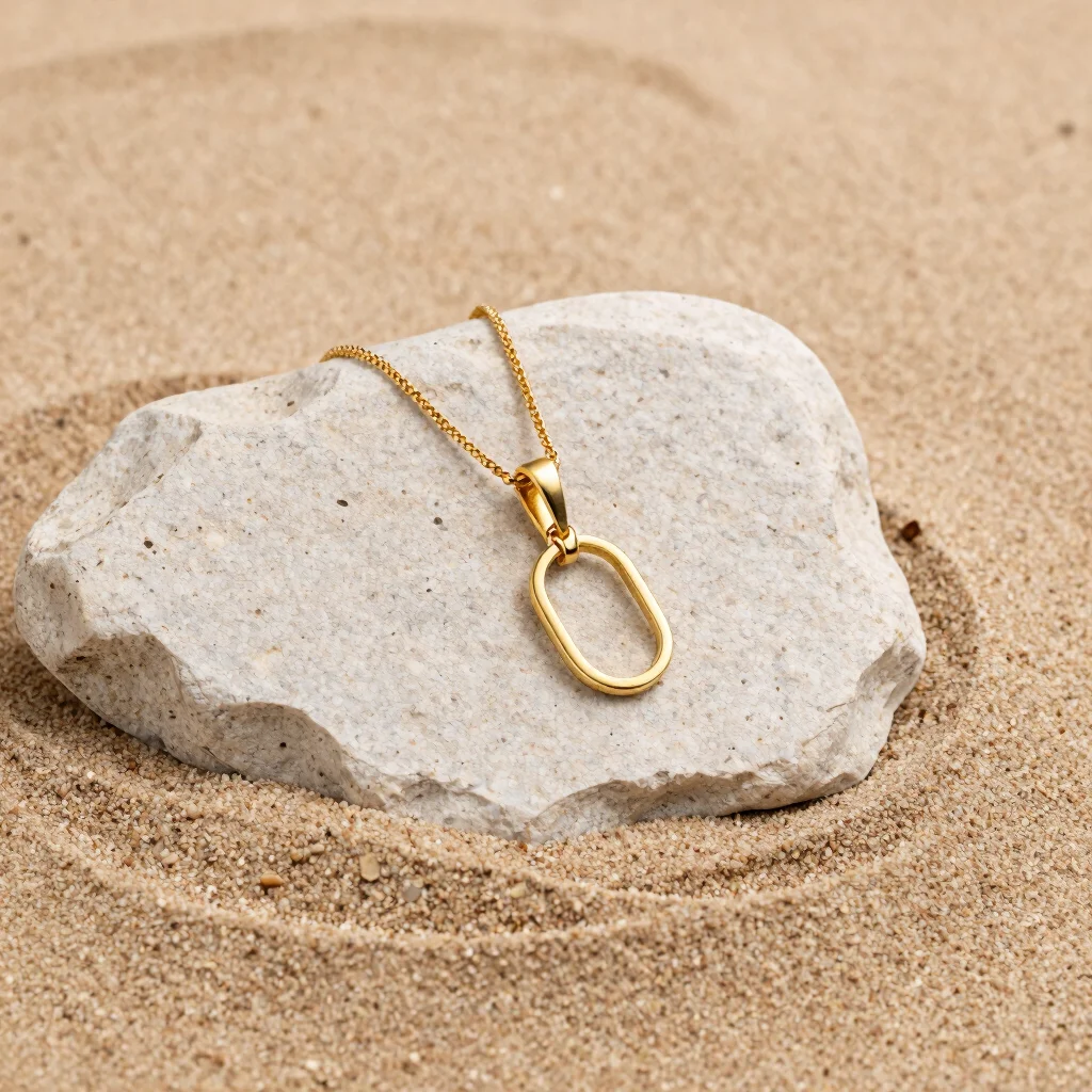 close-up shot of a minimalist gold-toned stainless steel pendant on smooth warm sandstone, soft neutral tones, fine jewe